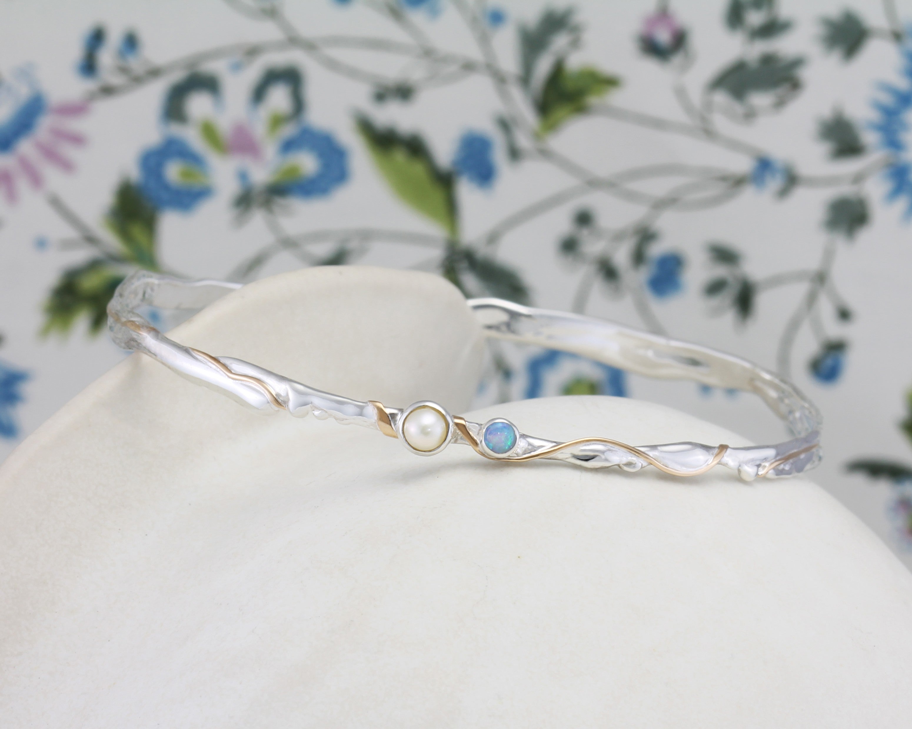 Silver bracelet with pearl and blue stone on a white pot with a floral background.