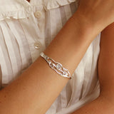 Silver bracelet on a wrist with a white blouse in the background