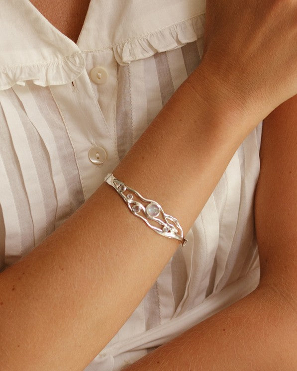 Silver bracelet on a wrist with a white blouse in the background