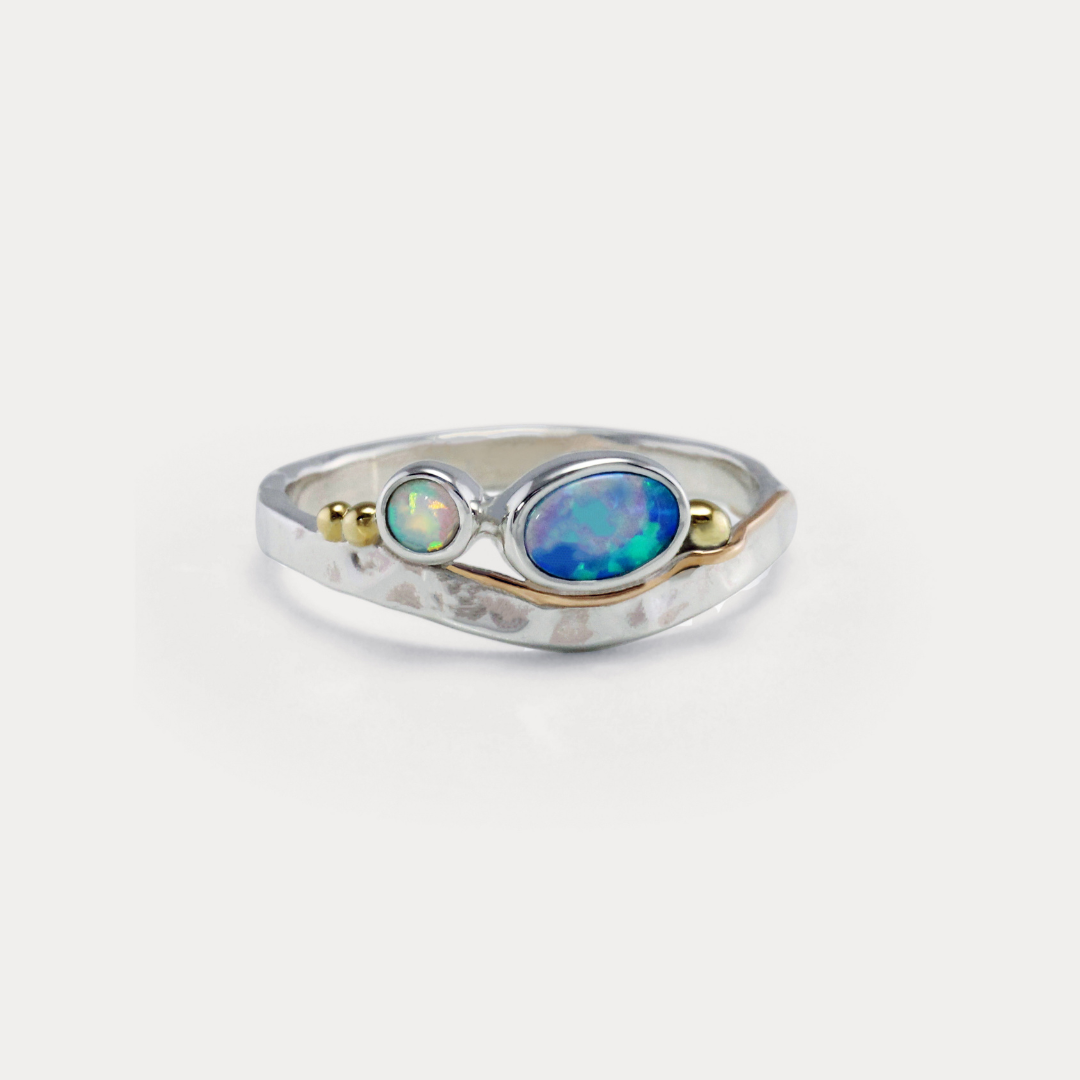 A Sterling Silver ring with a central blue-green Opal and white Opal accents, featuring gold flowing details on a hammered band.