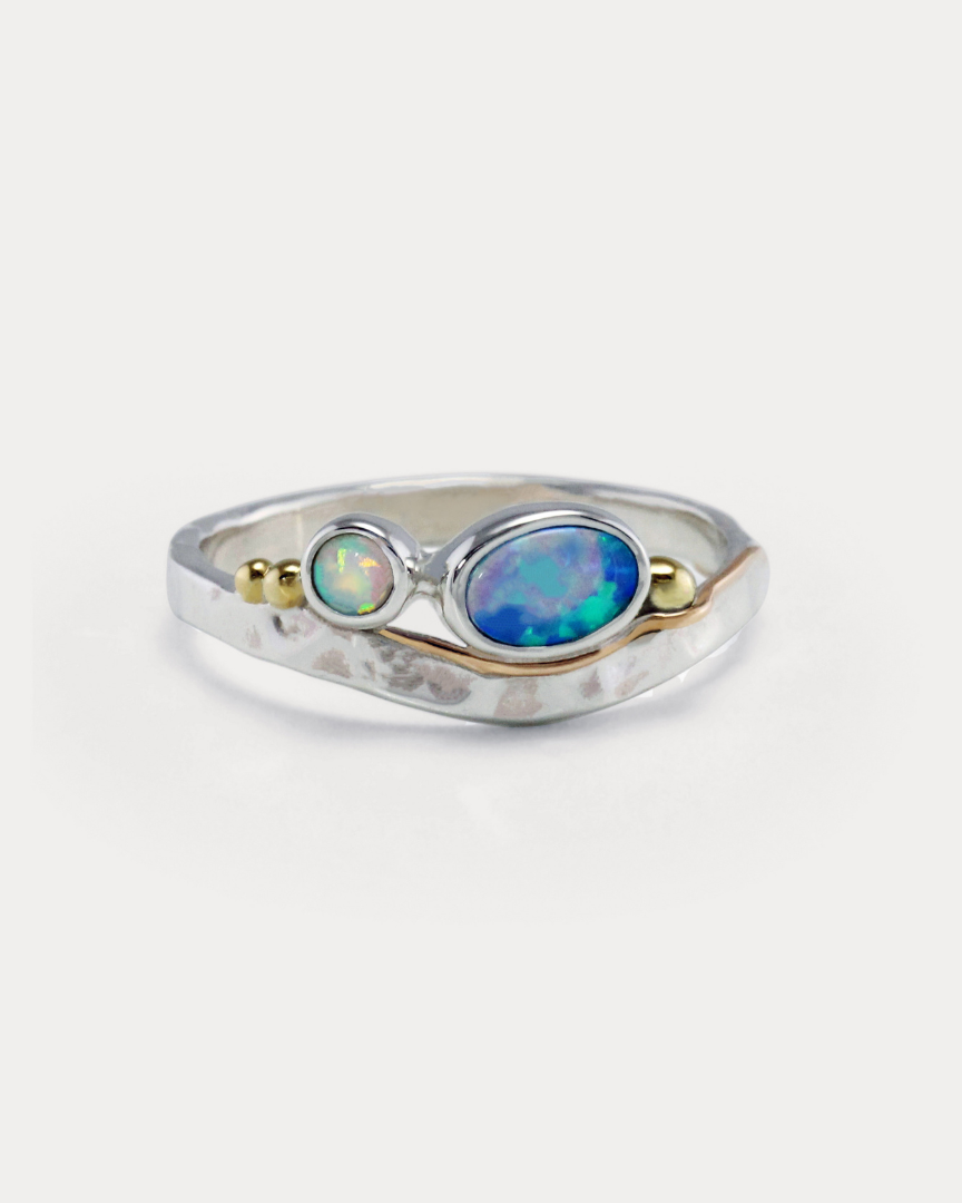 A Sterling Silver ring with a central blue-green Opal and white Opal accents, featuring gold flowing details on a hammered band.