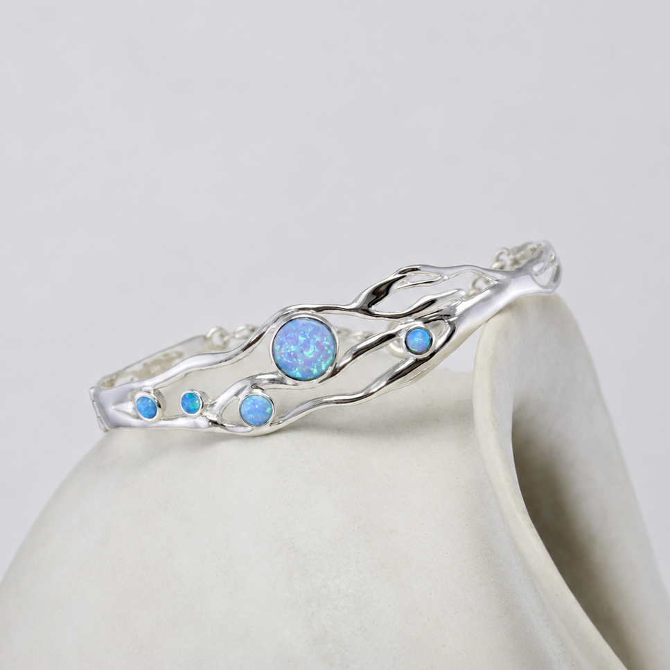 Silver bangle with blue opals on a white ceramic cup