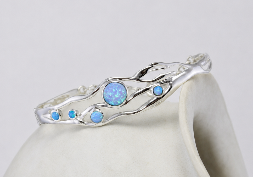 Silver bangle with blue opals on a white ceramic cup